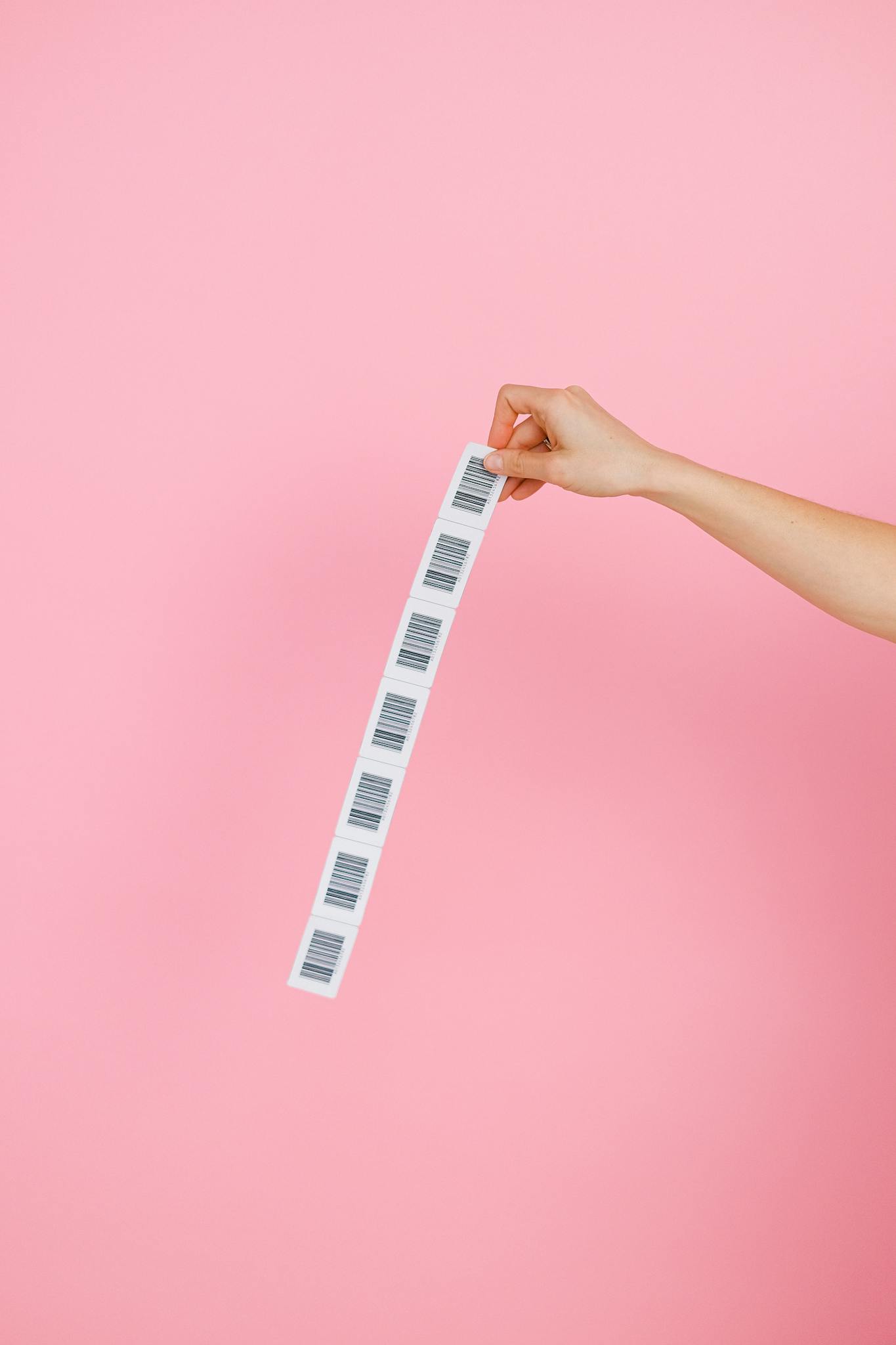 A hand holds a strip of barcodes against a pink background, creating a simple yet striking image.