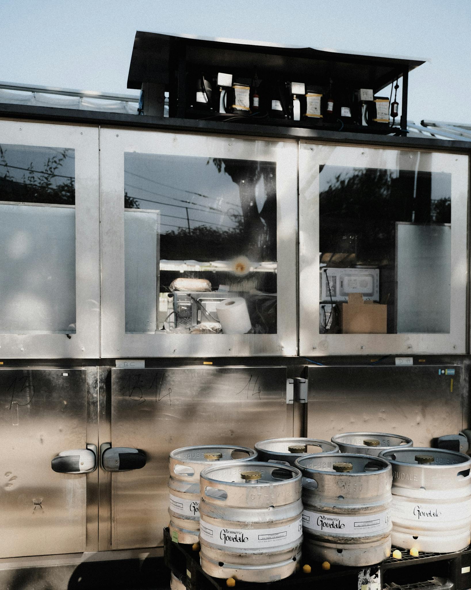 A collection of metal kegs outside a brewery storage unit on a sunny day.