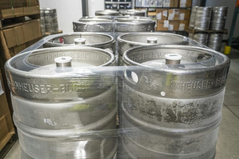 Metal beer kegs stacked and wrapped in plastic in a brewery warehouse, ready for distribution.