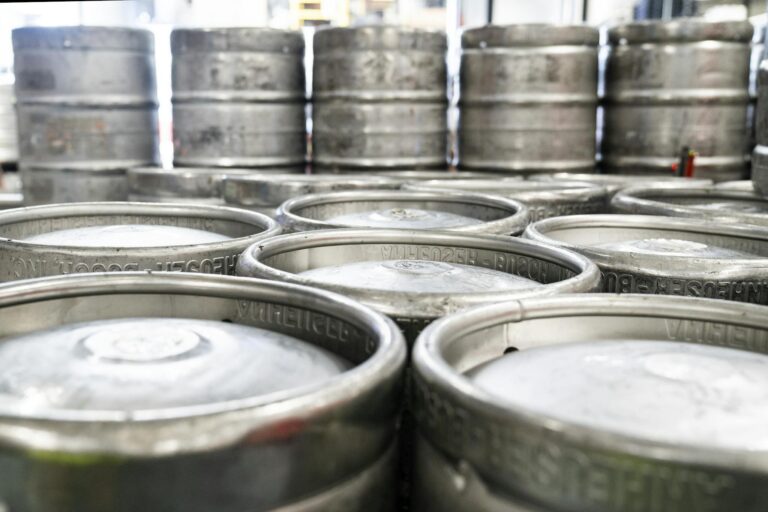 Rows of steel beer kegs stacked in a brewery warehouse ready for distribution.