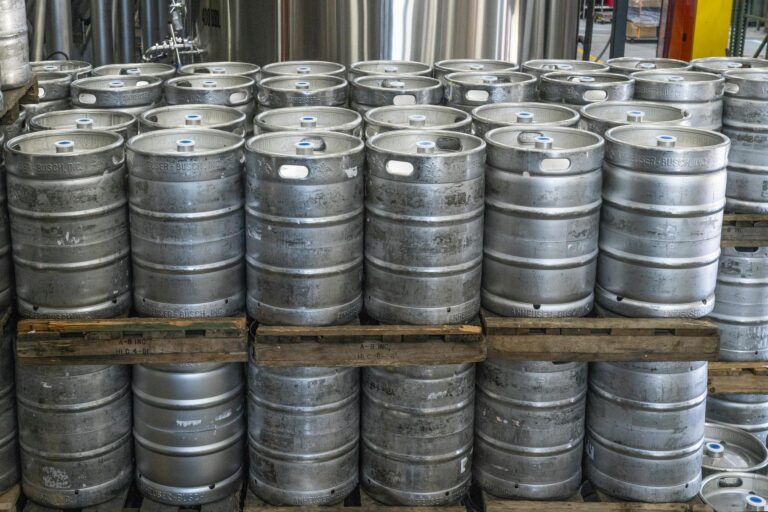 Steel kegs neatly stacked on pallets in an industrial brewery warehouse.